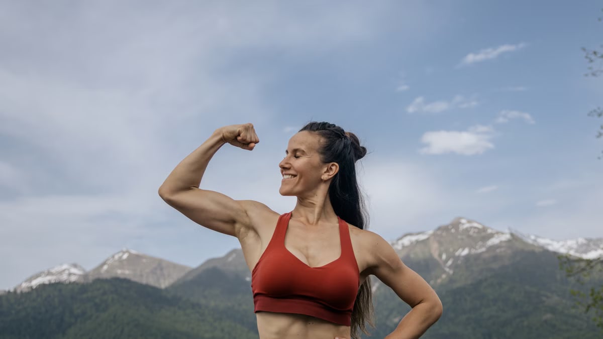 Woman in red sportswear flexing muscles against a scenic mountain backdrop.